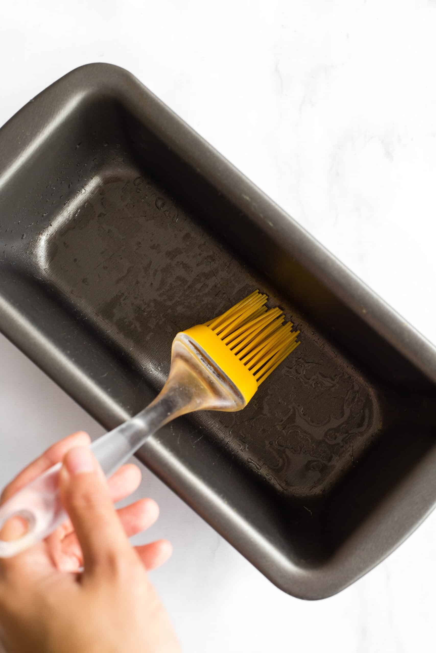 Using silicon brush to grease metal loaf pan.