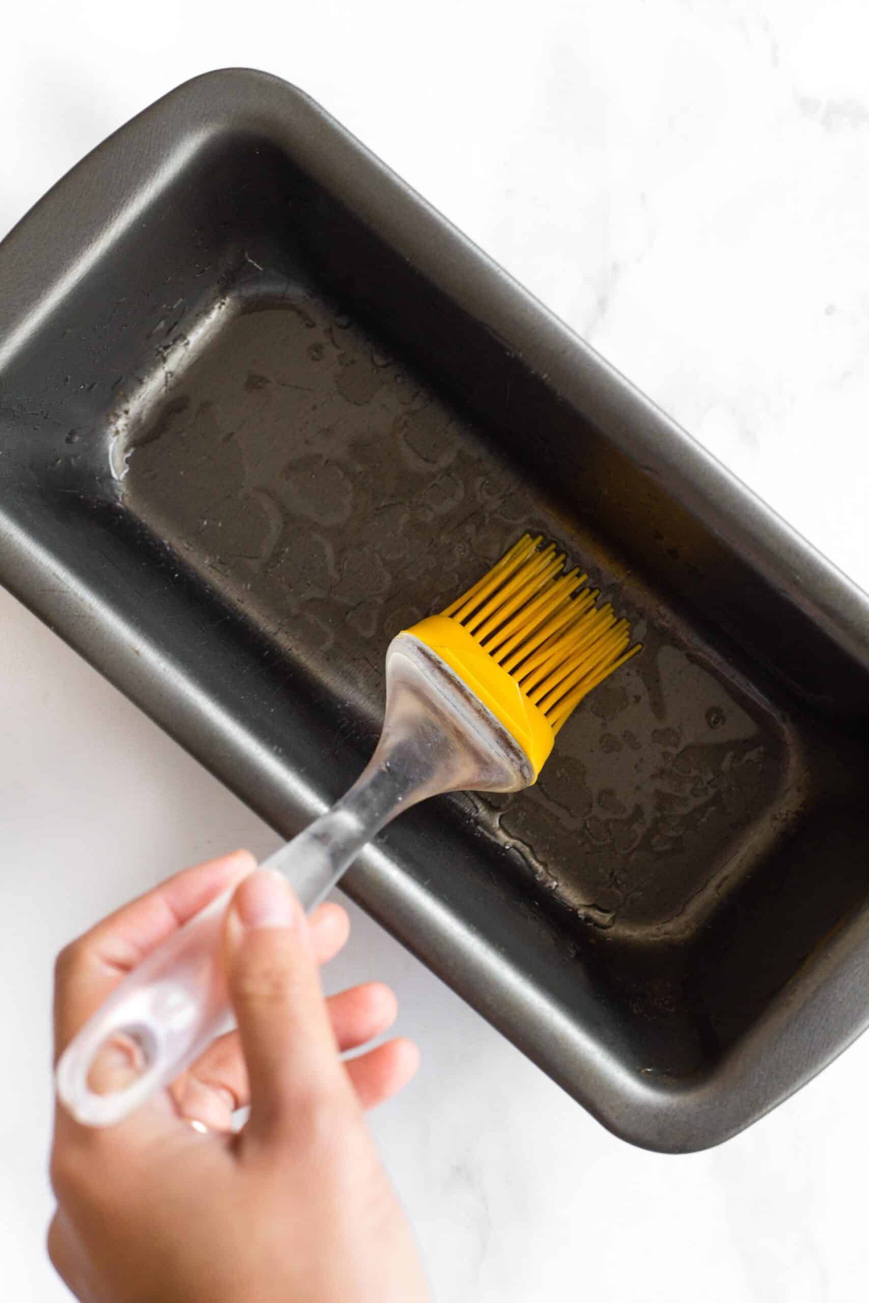 Using a brush to grease a metal loaf pan.