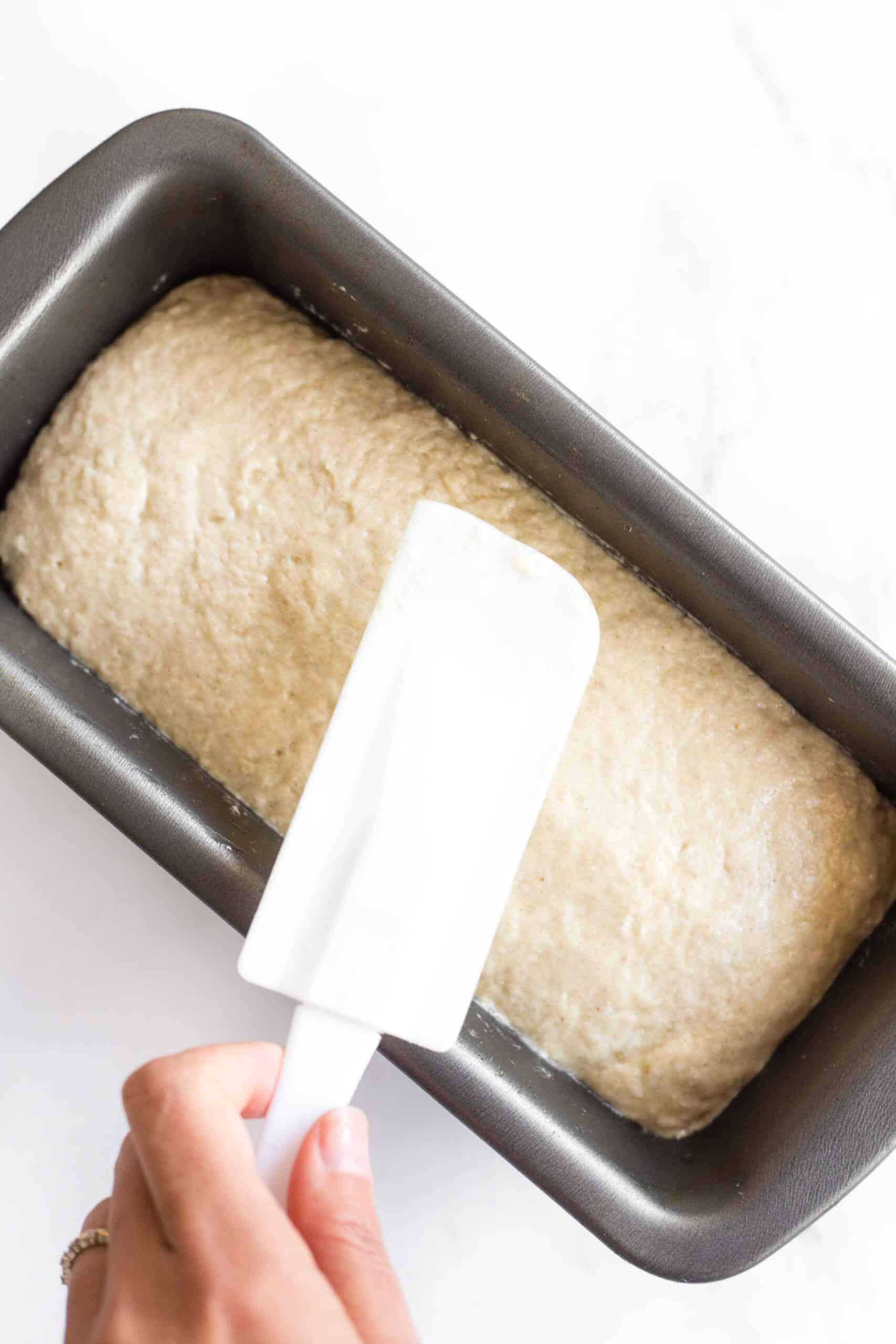 Using a wet spatula to smooth out the top of bread dough in loaf pan.