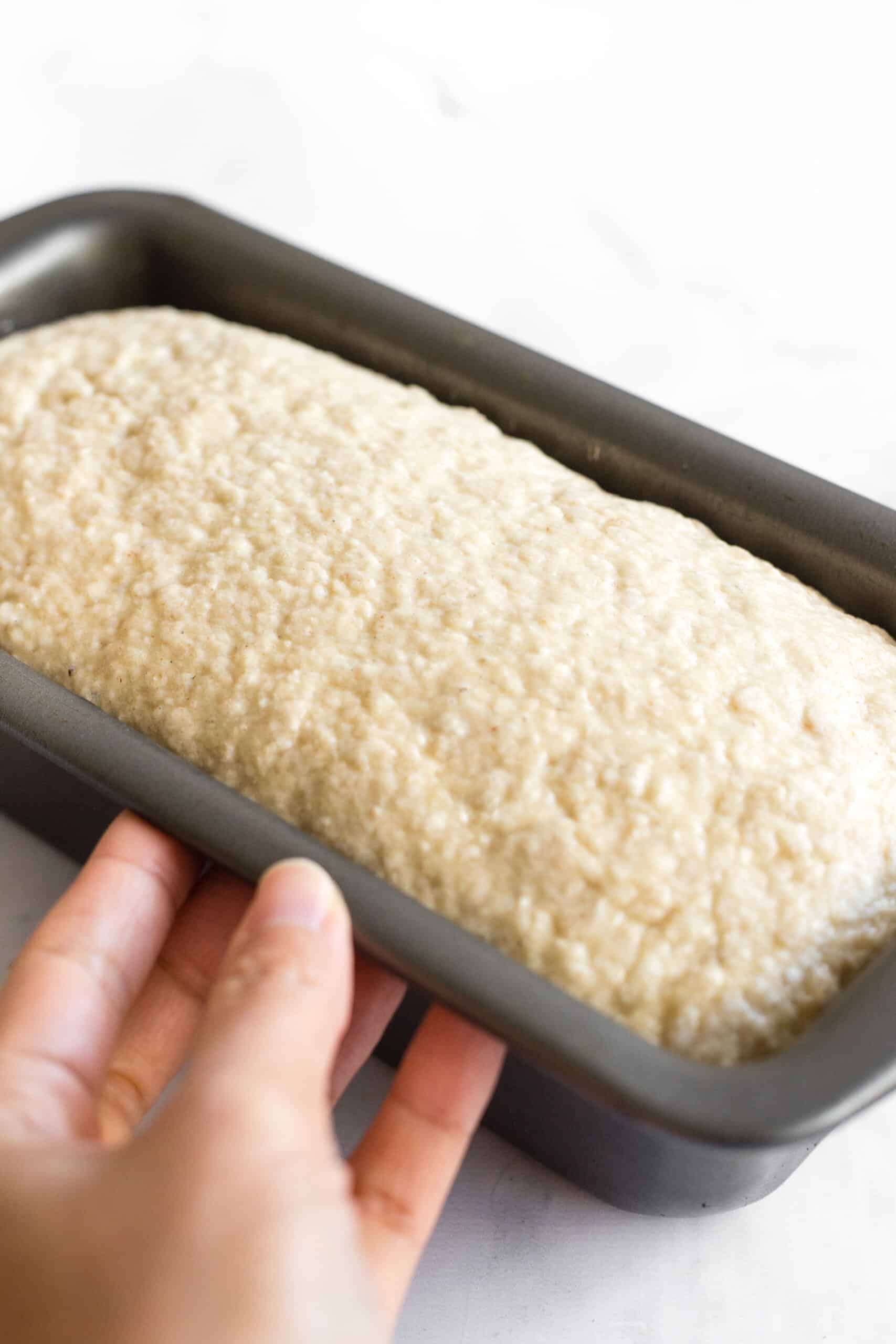 Holding a loaf pan with risen dough inside.