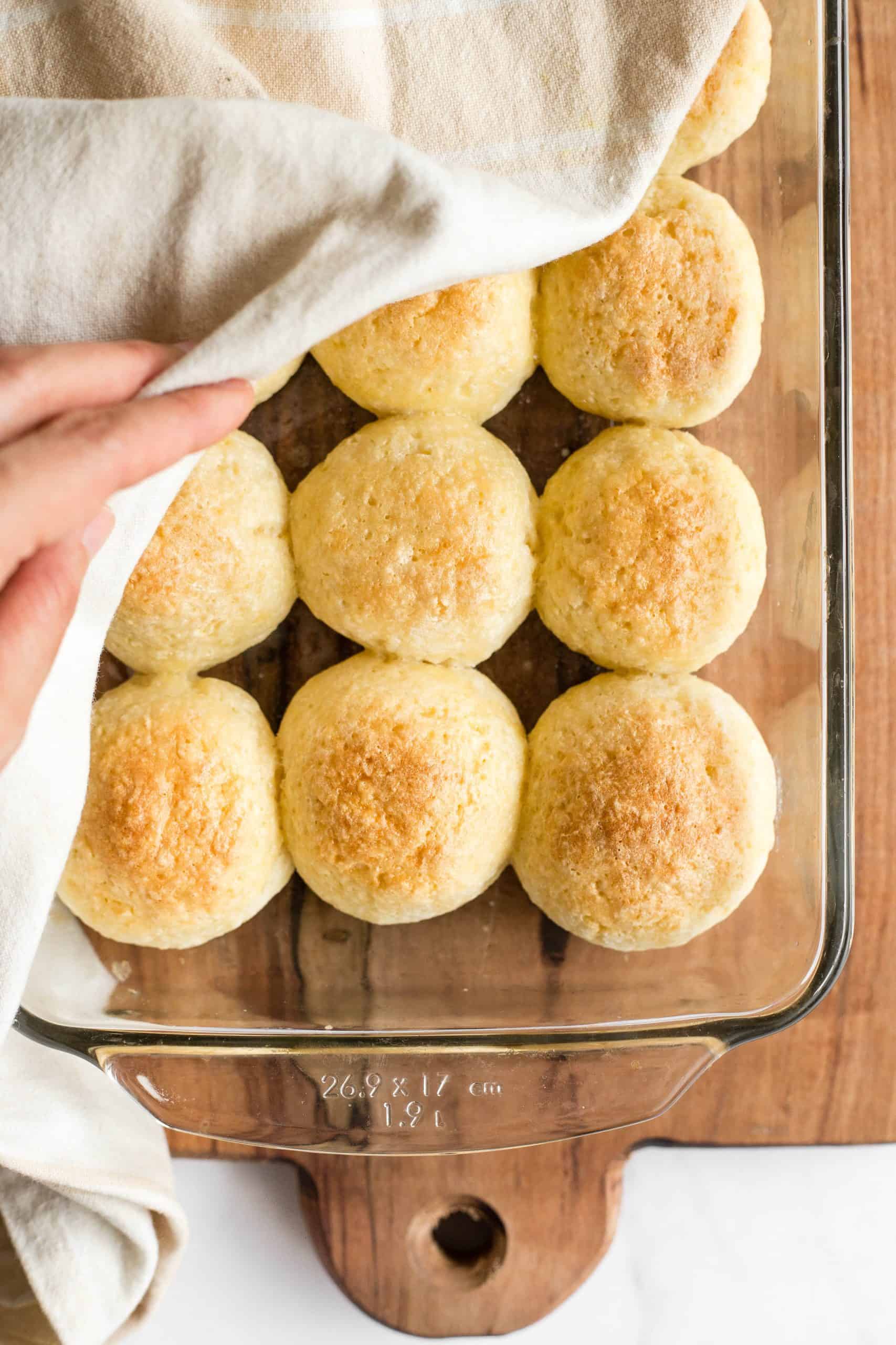 Removing a kitchen towel covering a glass pan full of dinner rolls.