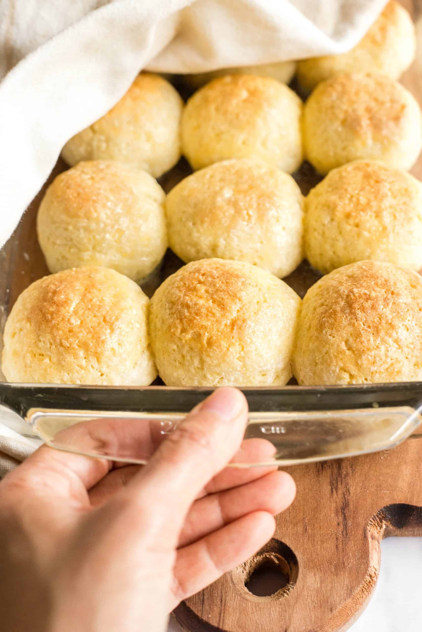 Hand holding a glass pan full of  gluten-free bread rolls.