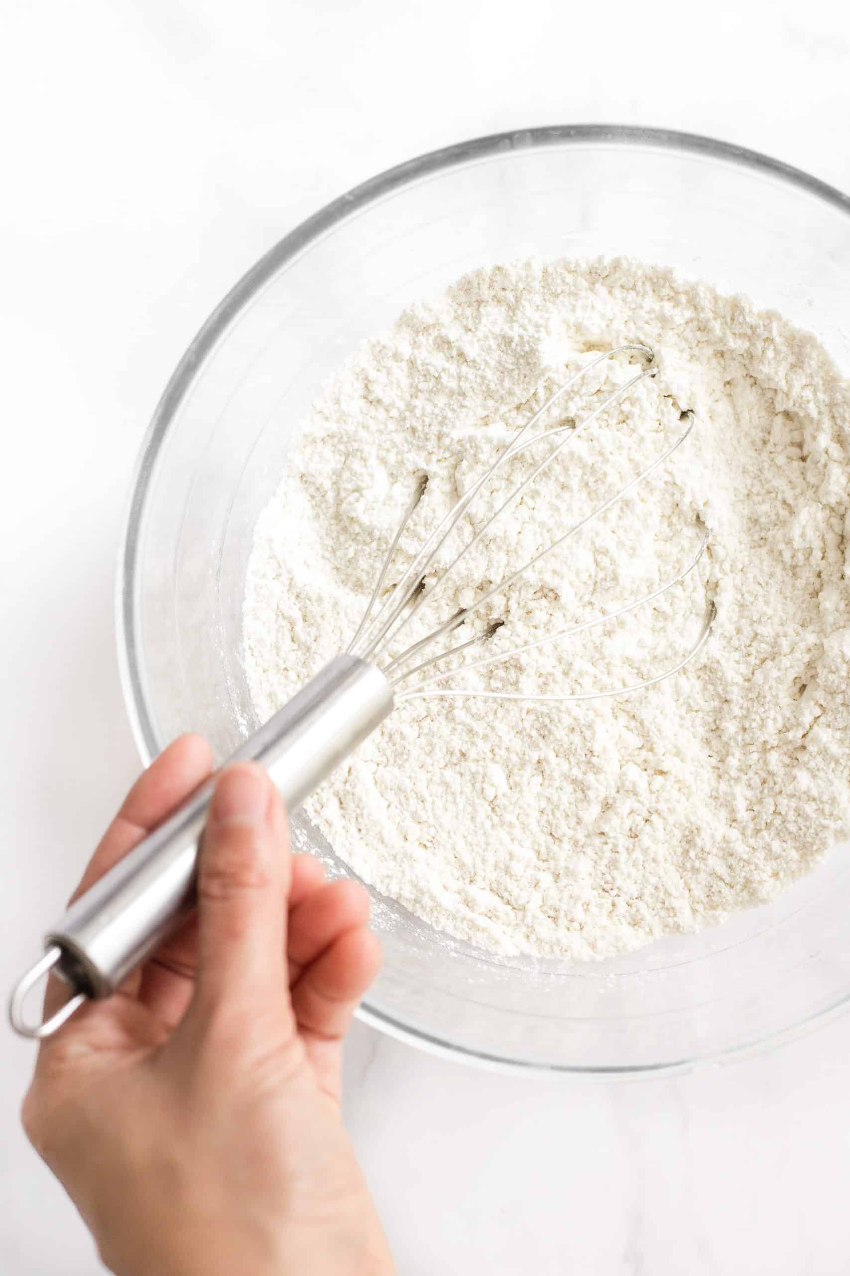 Hand whisking dry ingredients in a glass mixing bowl.
