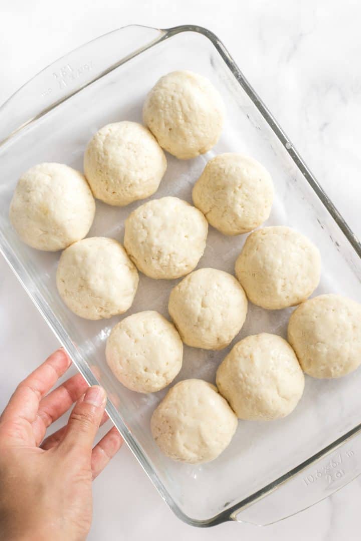 Hand holding glass pan with balls of gluten-free bread dough.