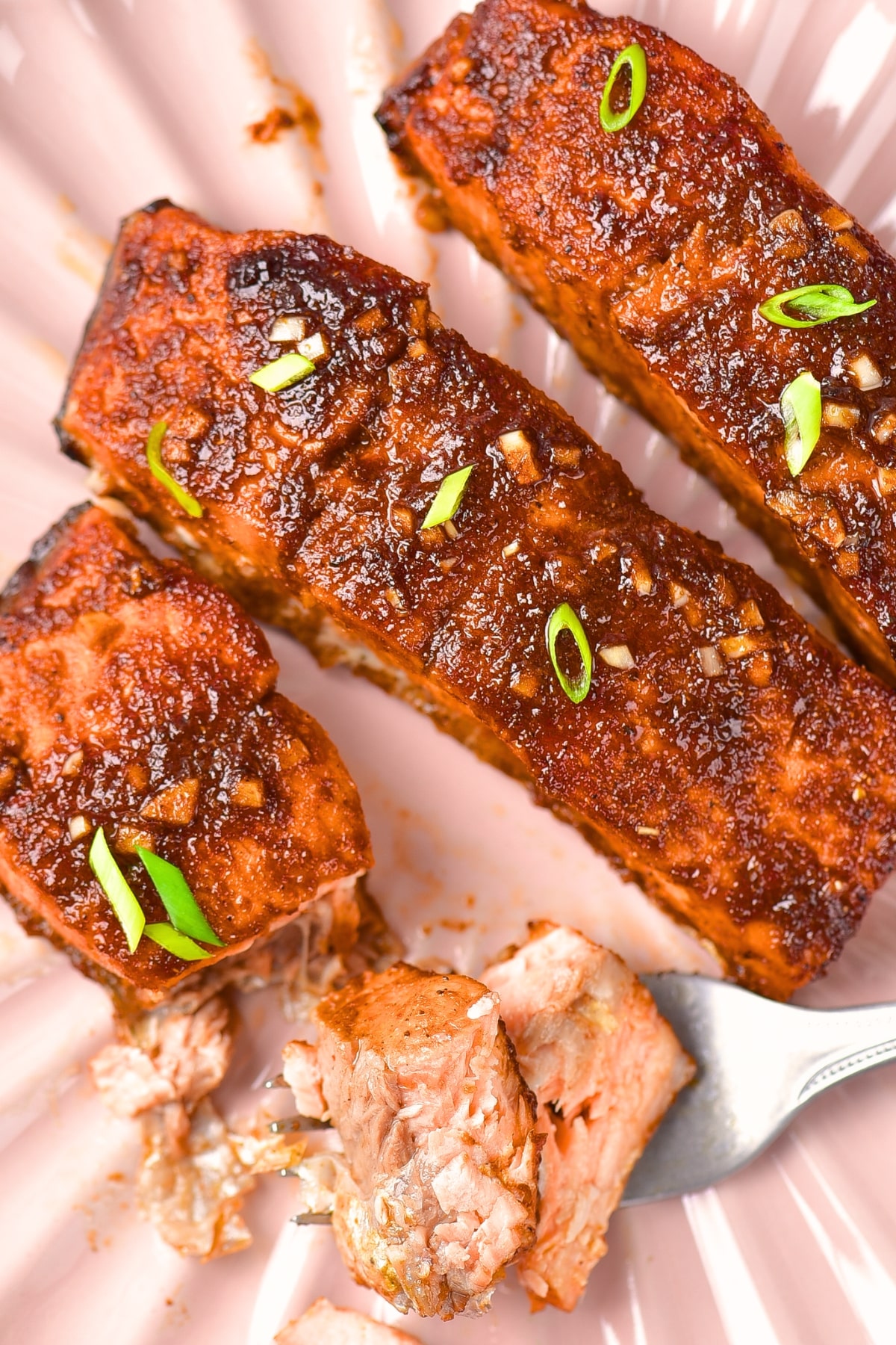 Top down view of baked spicy firecracker salmon on pink plate.