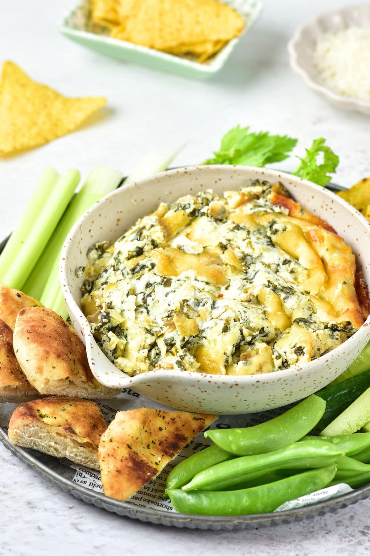 A bowl of spinach and artichoke dip with pita chips and raw veggies
