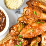 Top down view of sticky chicken wings sprinkled with sesame seeds and green onions
