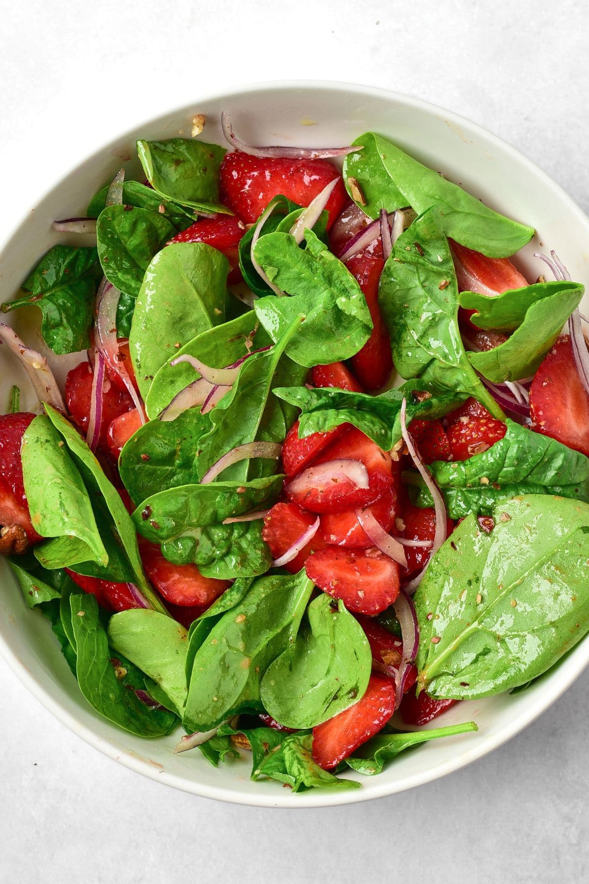 Top down view of a bowl of spinach leaves, sliced strawberries, sliced red onions