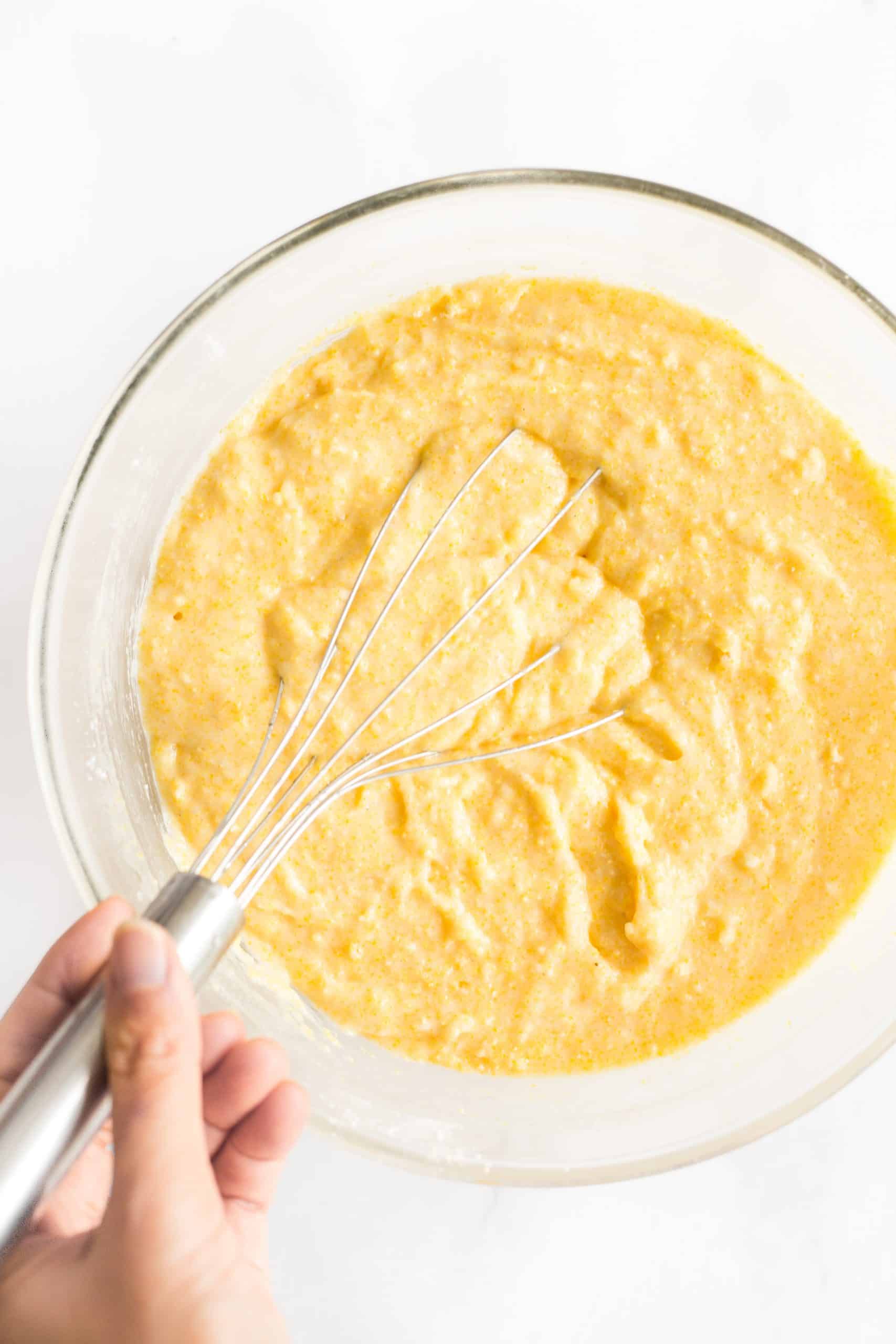 Top down view of hand whisking gluten-free cornbread muffin batter in a bowl.