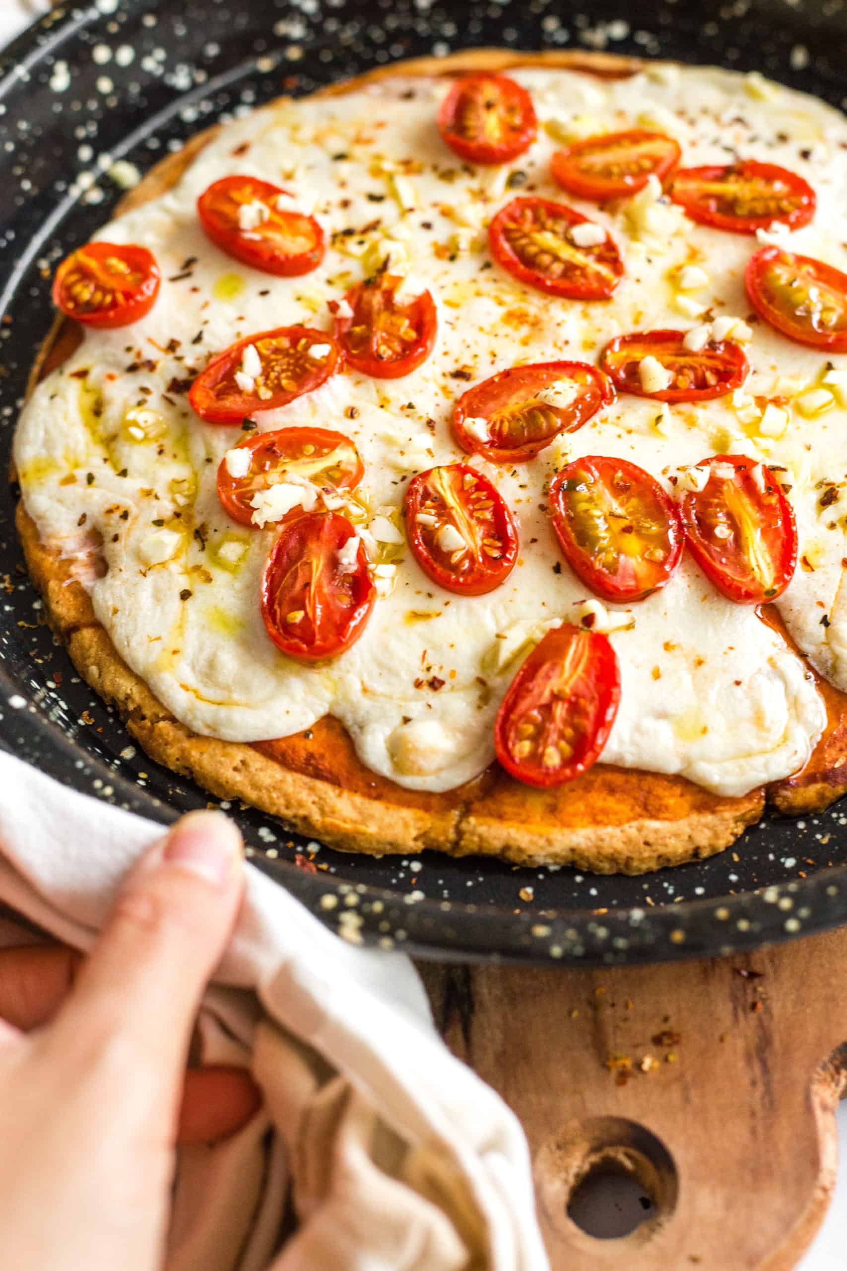 Gluten-free pizza topped with cheese and cherry tomatoes in a pizza pan