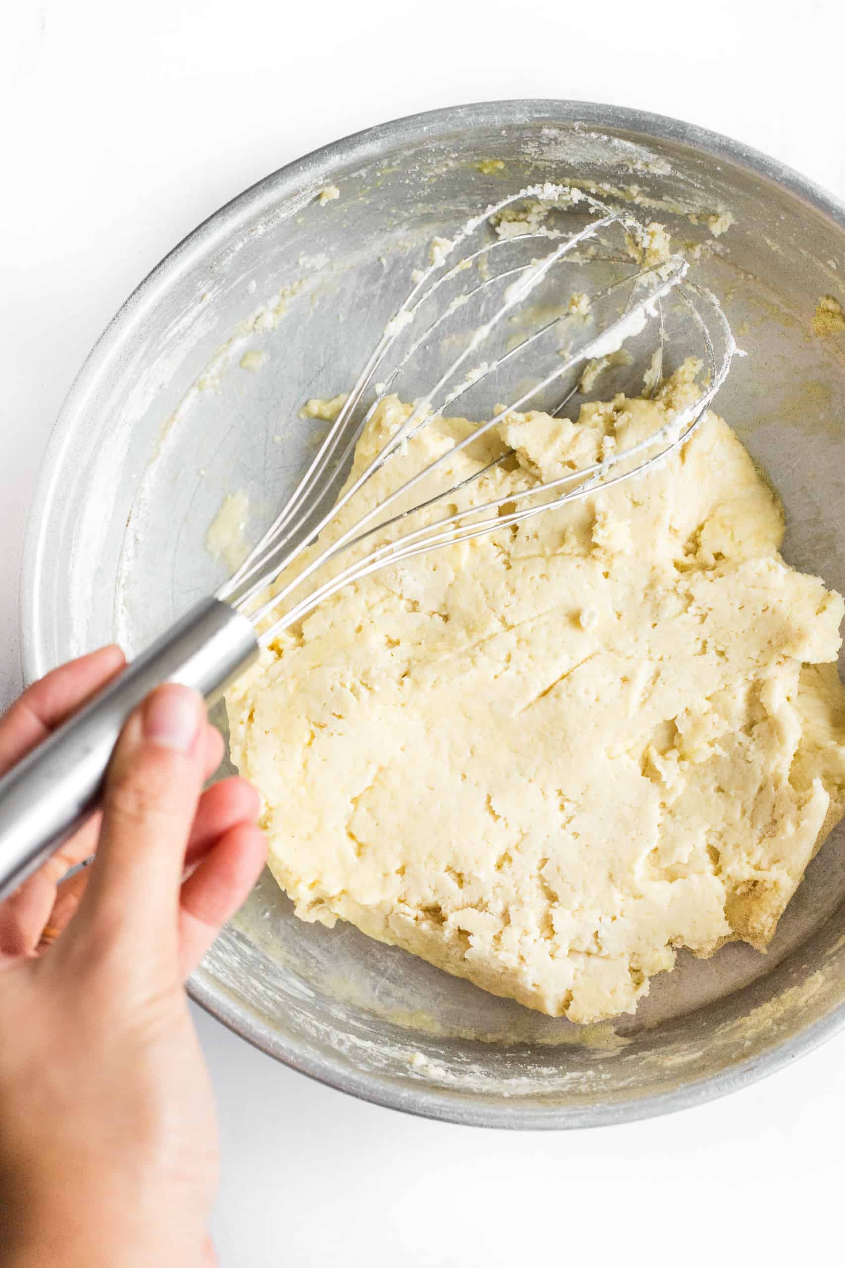 Mixing gluten-free pizza crust dough in a large metal bowl.