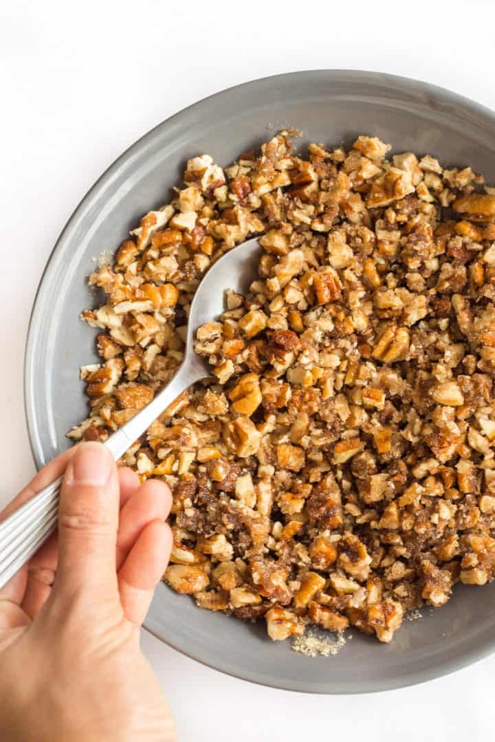 Hand holding a spoon in a bowl of chopped pecans.