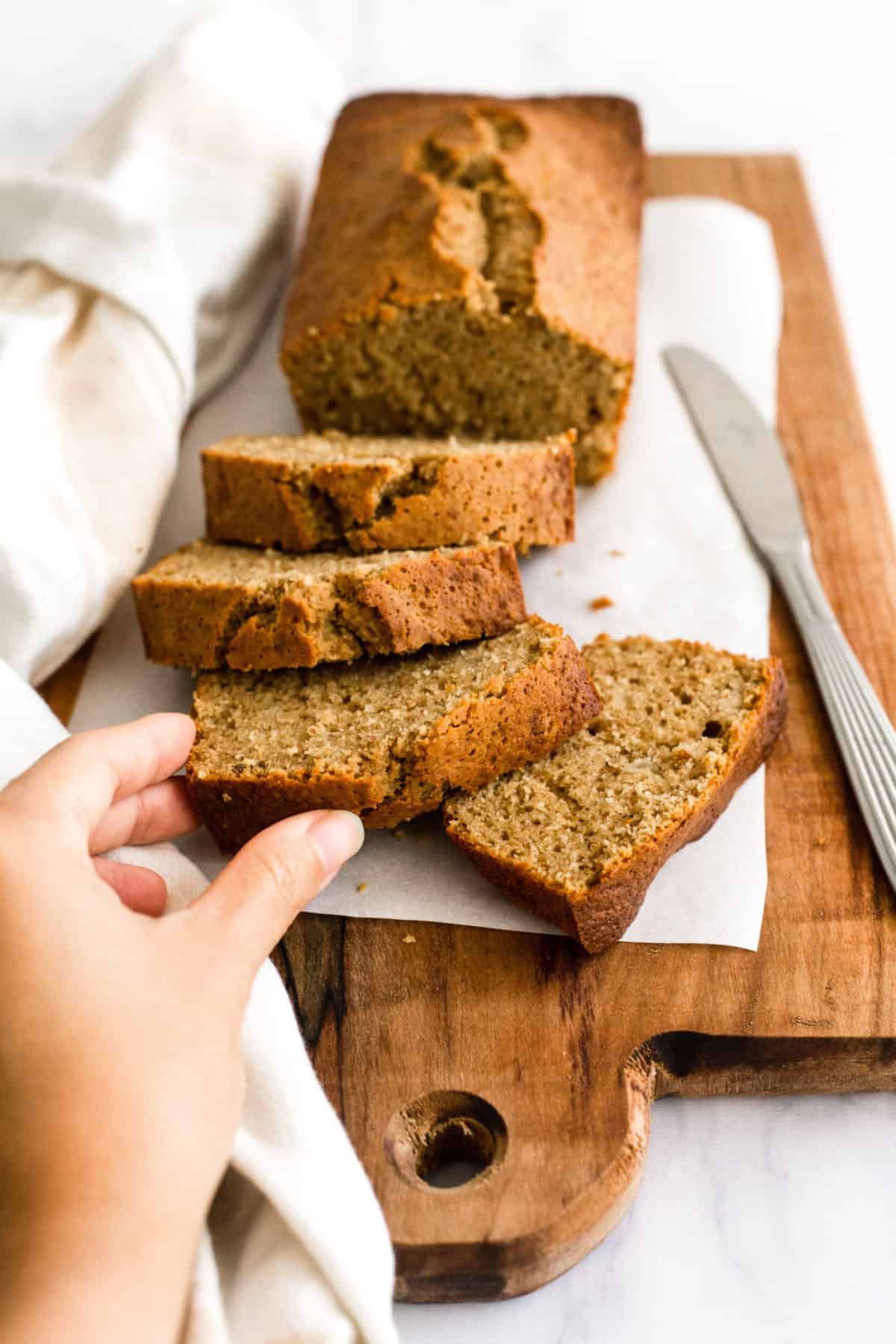 Hand reaching for a slice of gluten-free banana bread.