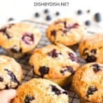 Hand reaching for a blueberry muffin on a wire rack.