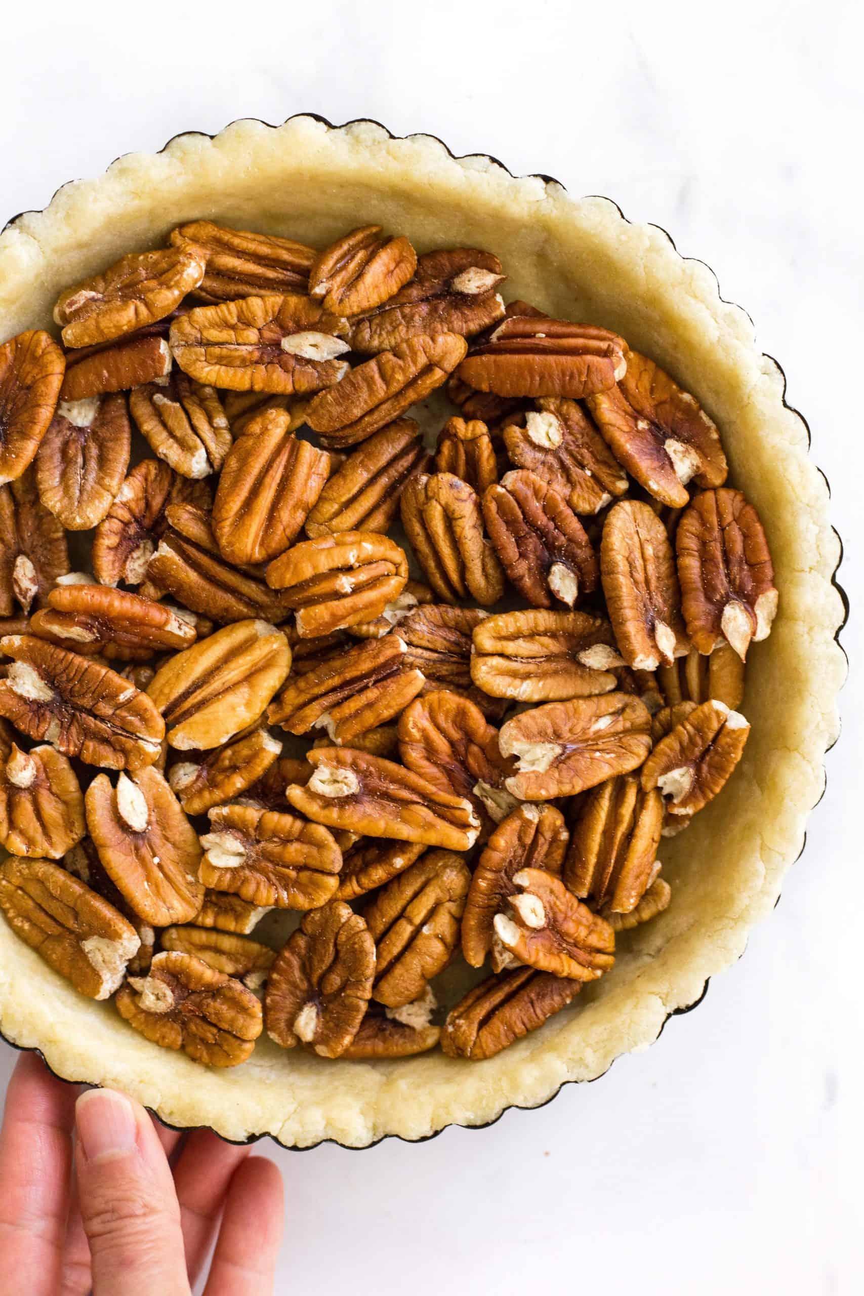 Hand holding a pie tin with unbaked pie crust filled with pecans.