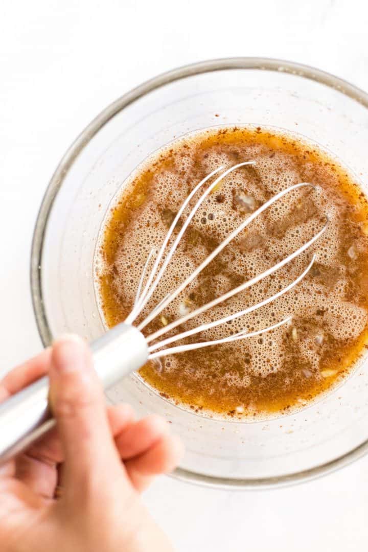 Whisking a brown liquid mixture in glass bowl.