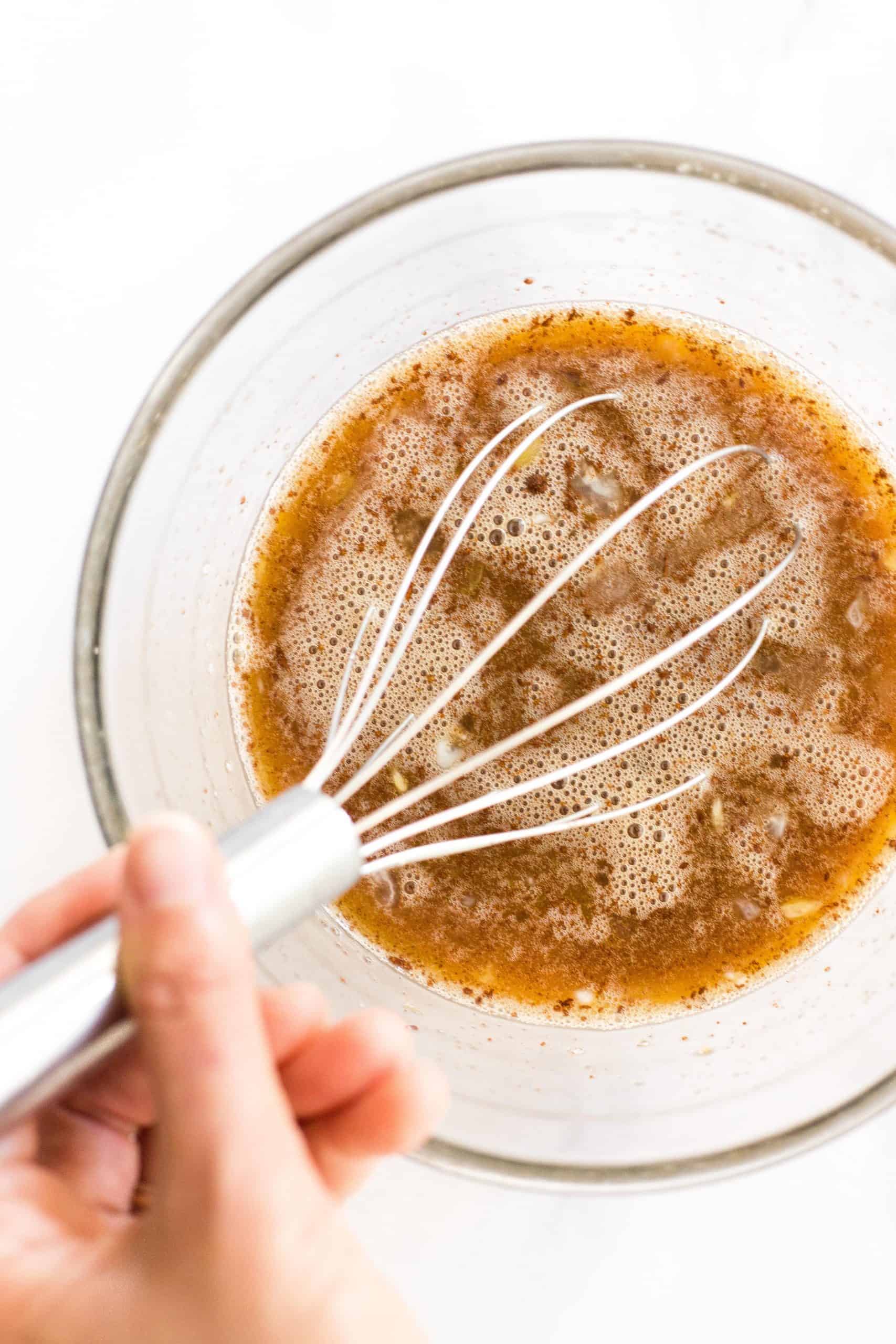 Whisking a brown liquid mixture in a glass mixing bowl.