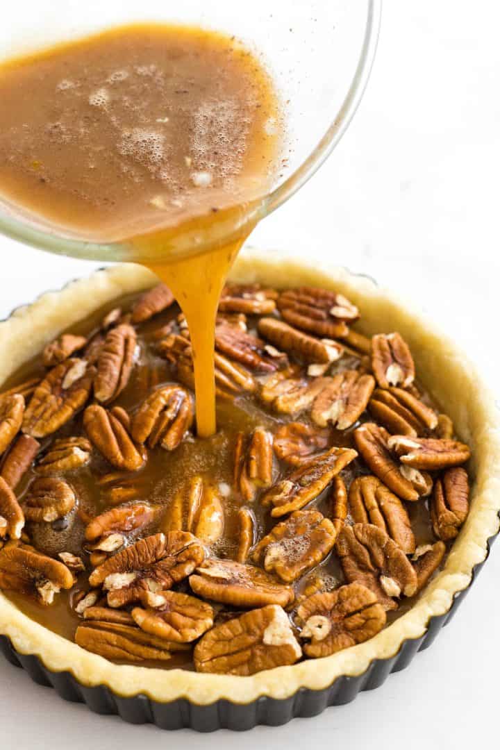 Pouring brown liquid mixture over pecans in pie crust