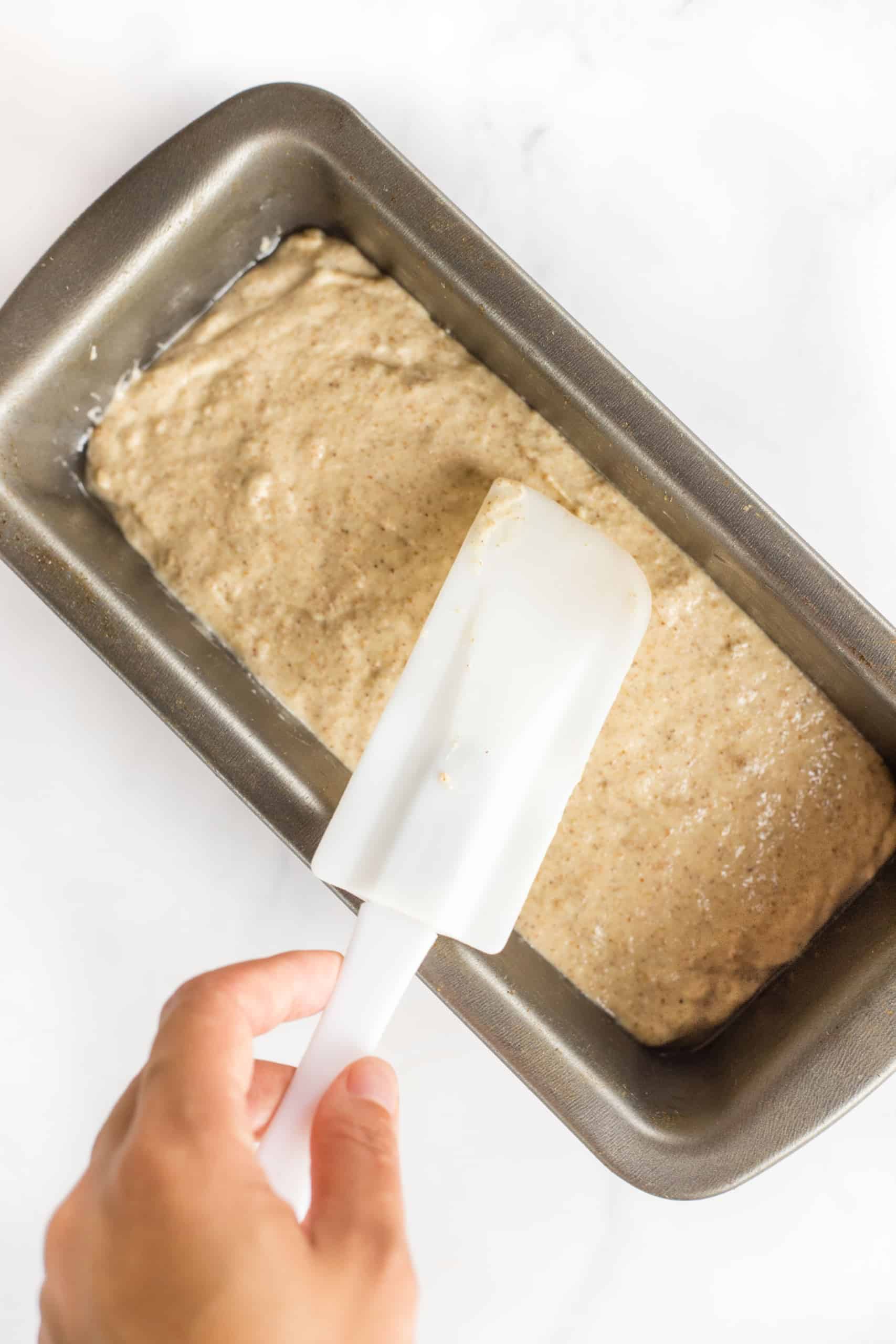 Using a spatula to smooth out the top of bread batter in a loaf pan.