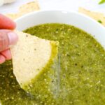 Dipping a corn nacho into a bowl of green tomatillo sauce