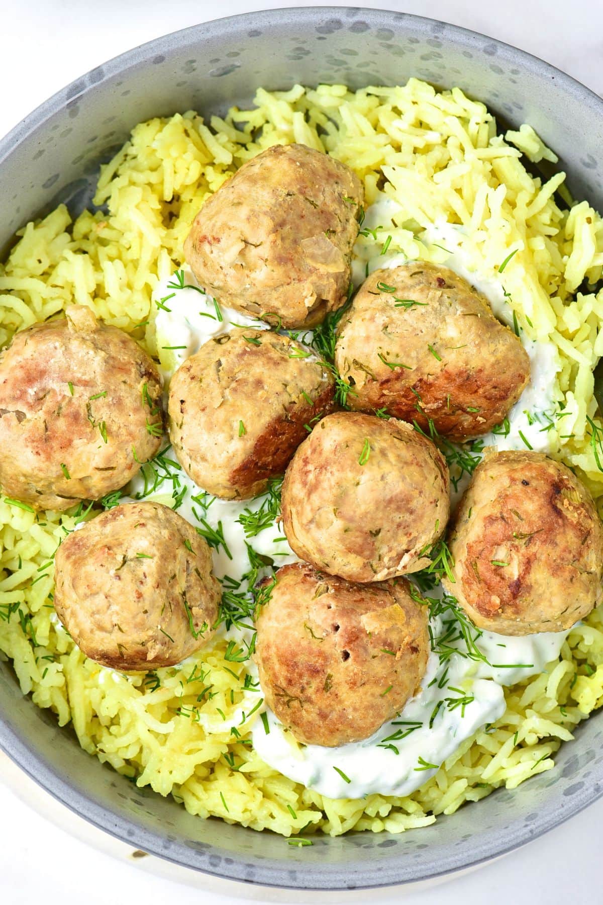 Top down view of a bowl of rice, feta turkey meatballs, and fresh dill.