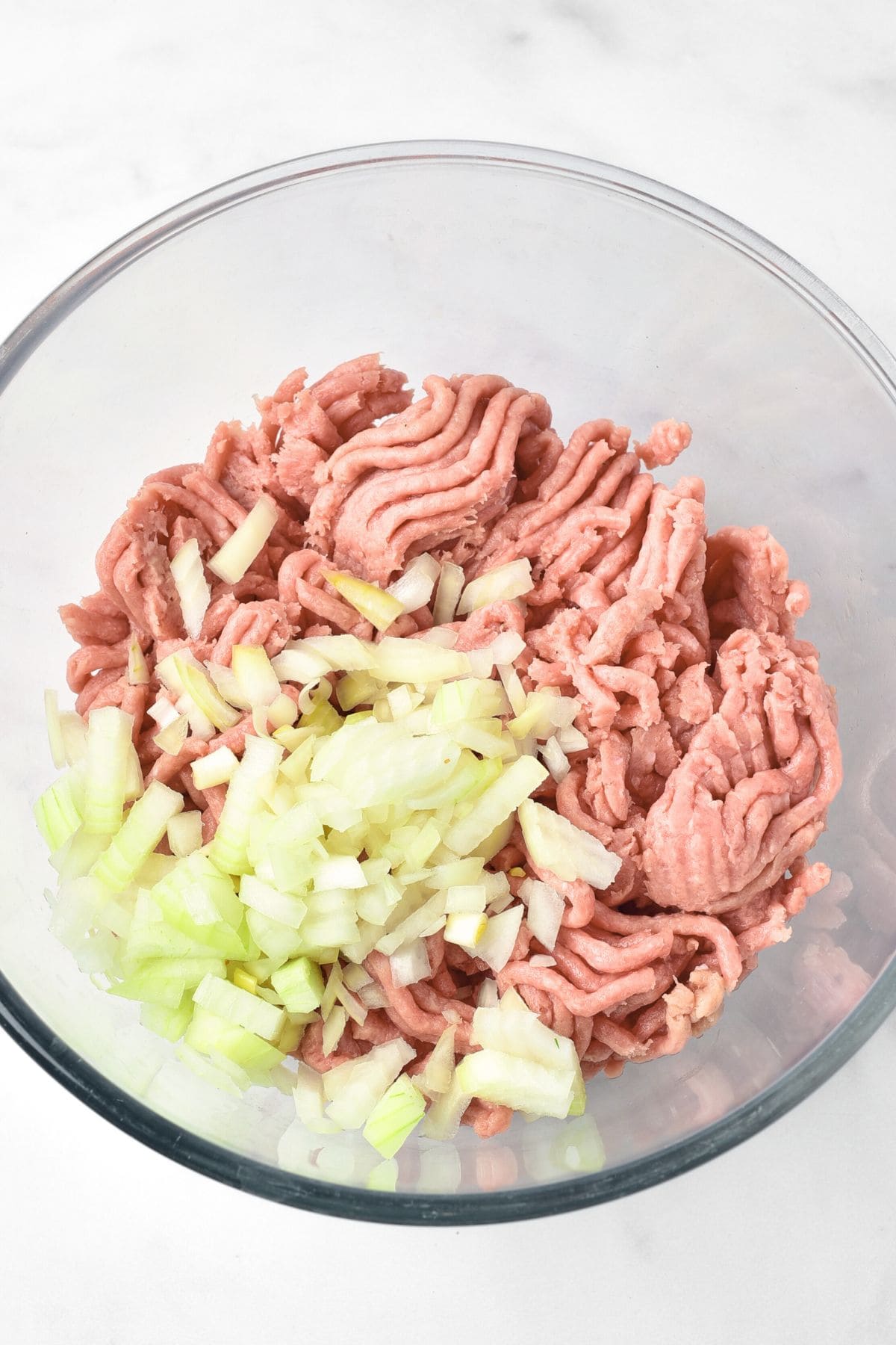 A glass bowl with diced onions and ground turkey.