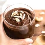 Up close shot of hand holding a glass of chocolate pudding.