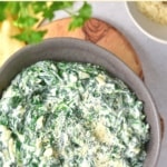 Top down view of a bowl of spinach dip on wooden board.