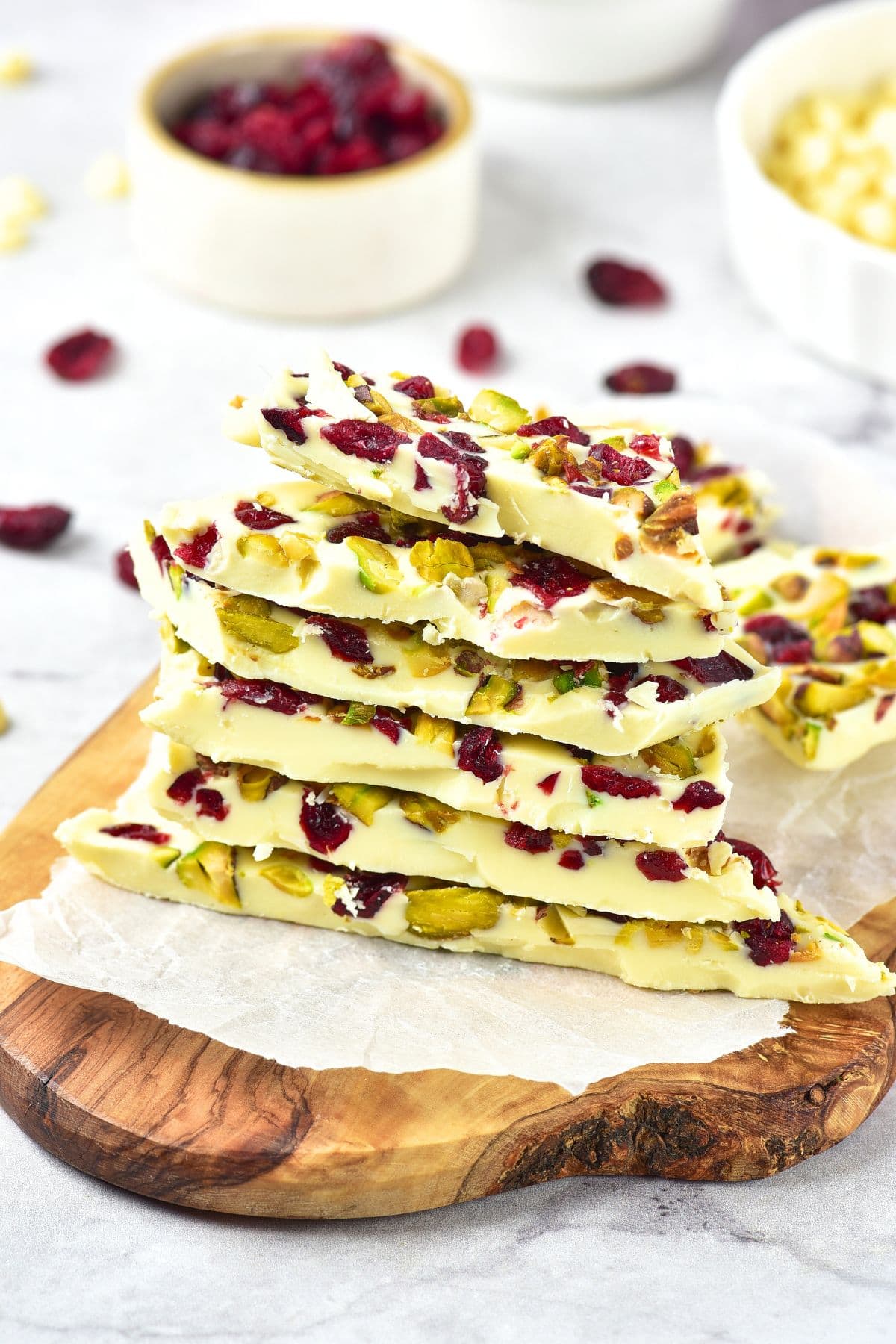 A stack of white chocolate cranberry bark on wooden board.