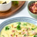 A bowl of tuscan soup garnished with bacon crumbles and herbs