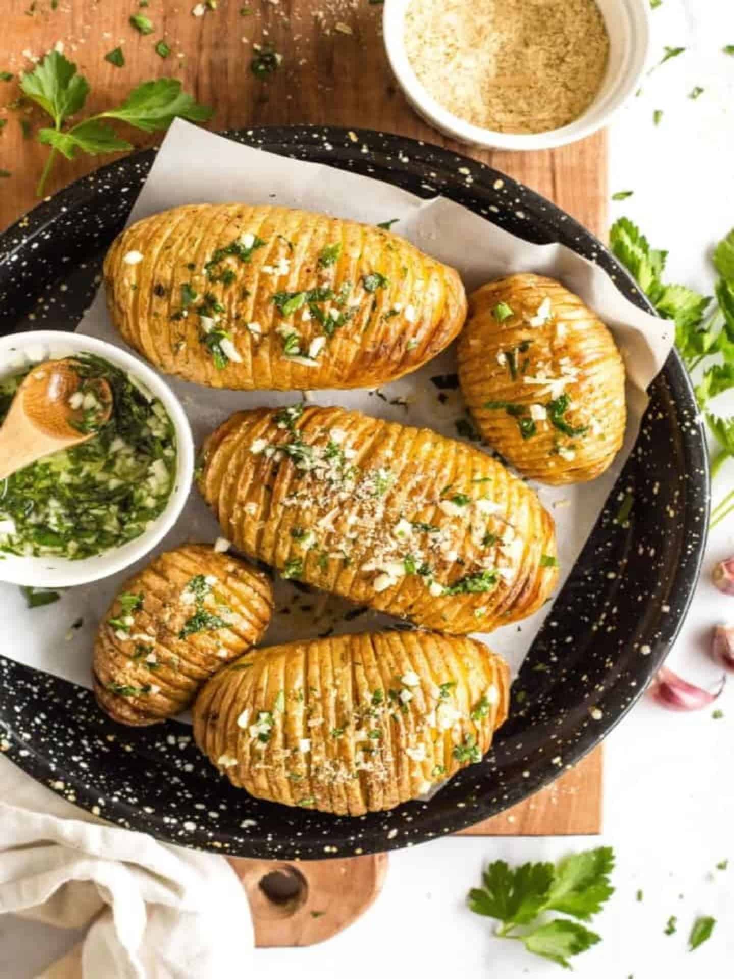 resized image of hasselback potatoes with parsley and garlic sauce on a black dish