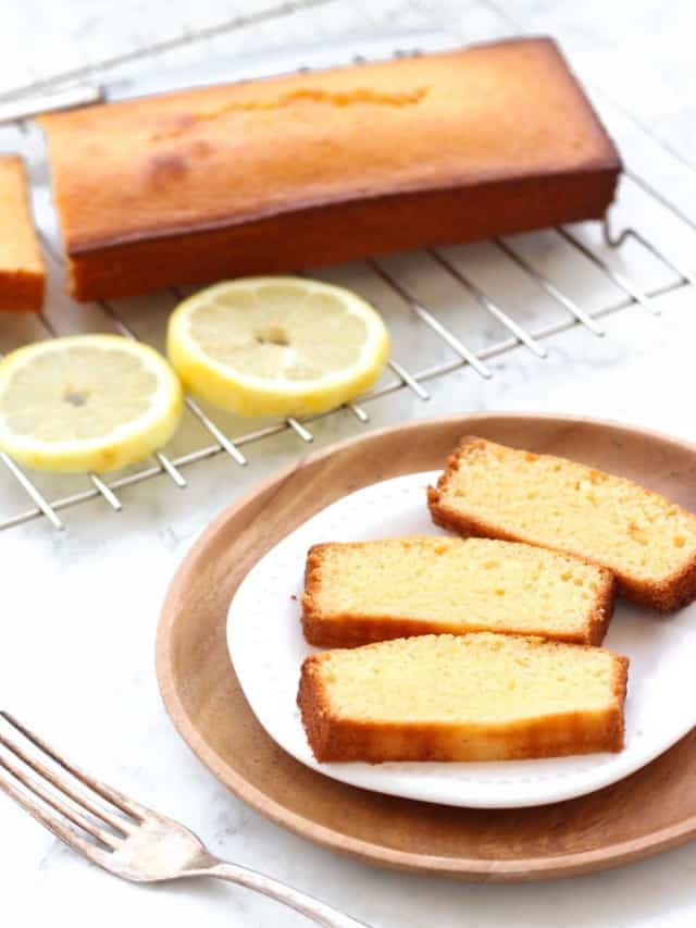 resized image of sliced lemon cake on white plate with cake and lemon slices on silver rack